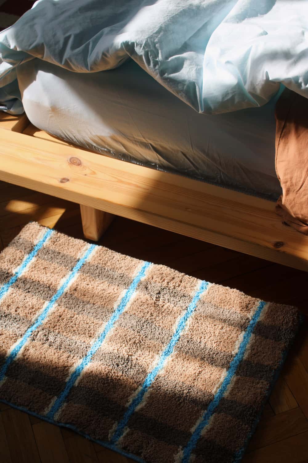 Brown checkered bath mat with blue stripes in front of a wooden bed.