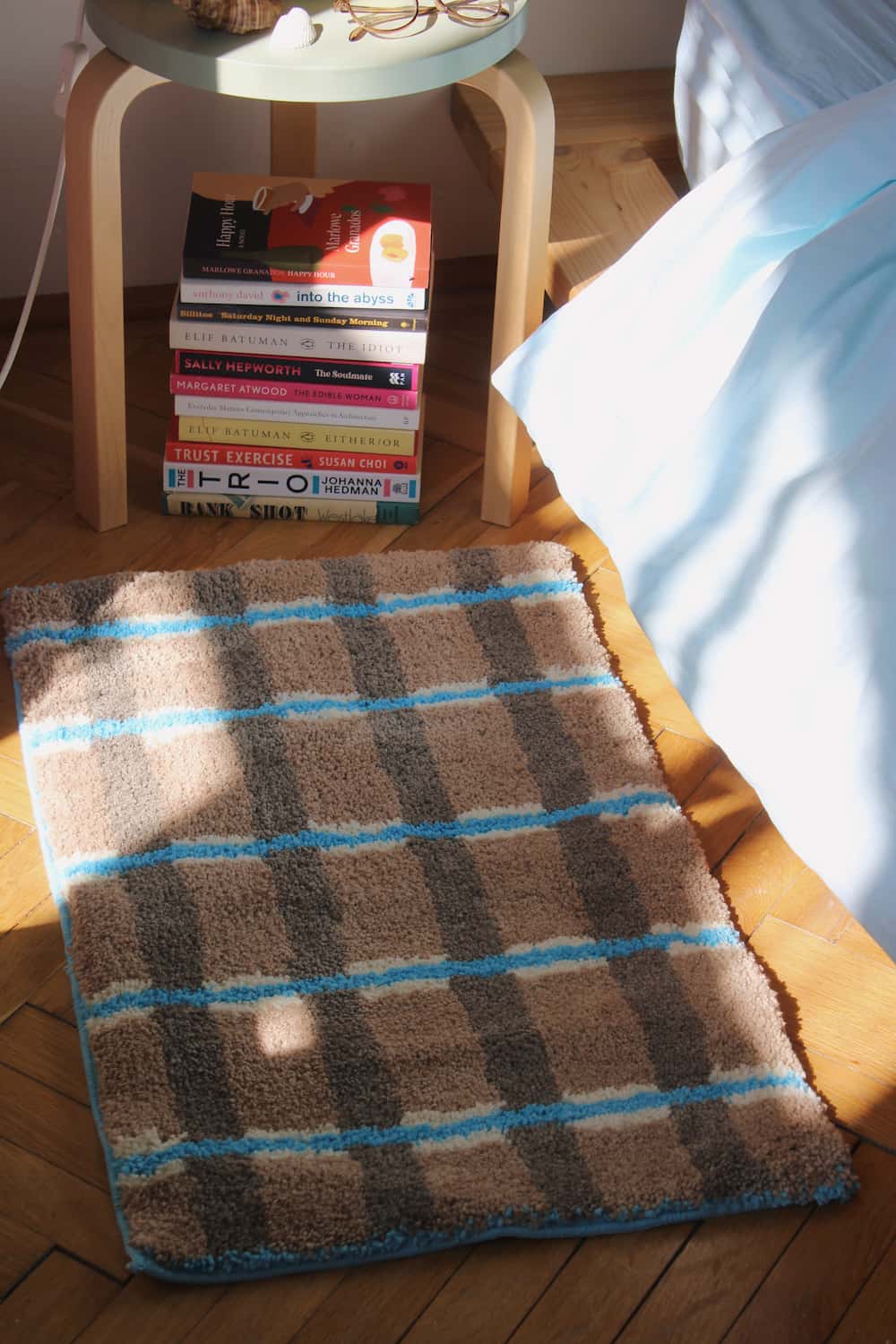 Plaid rug on a wooden floor with books stacked against a wall.