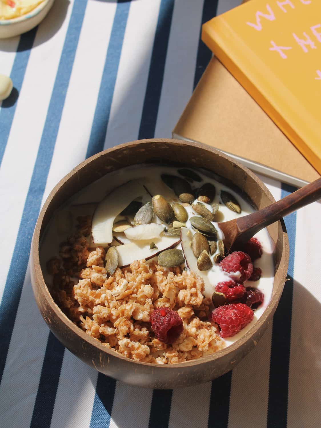 Nari coconut bowl with granola on a striped table next to a stack of books