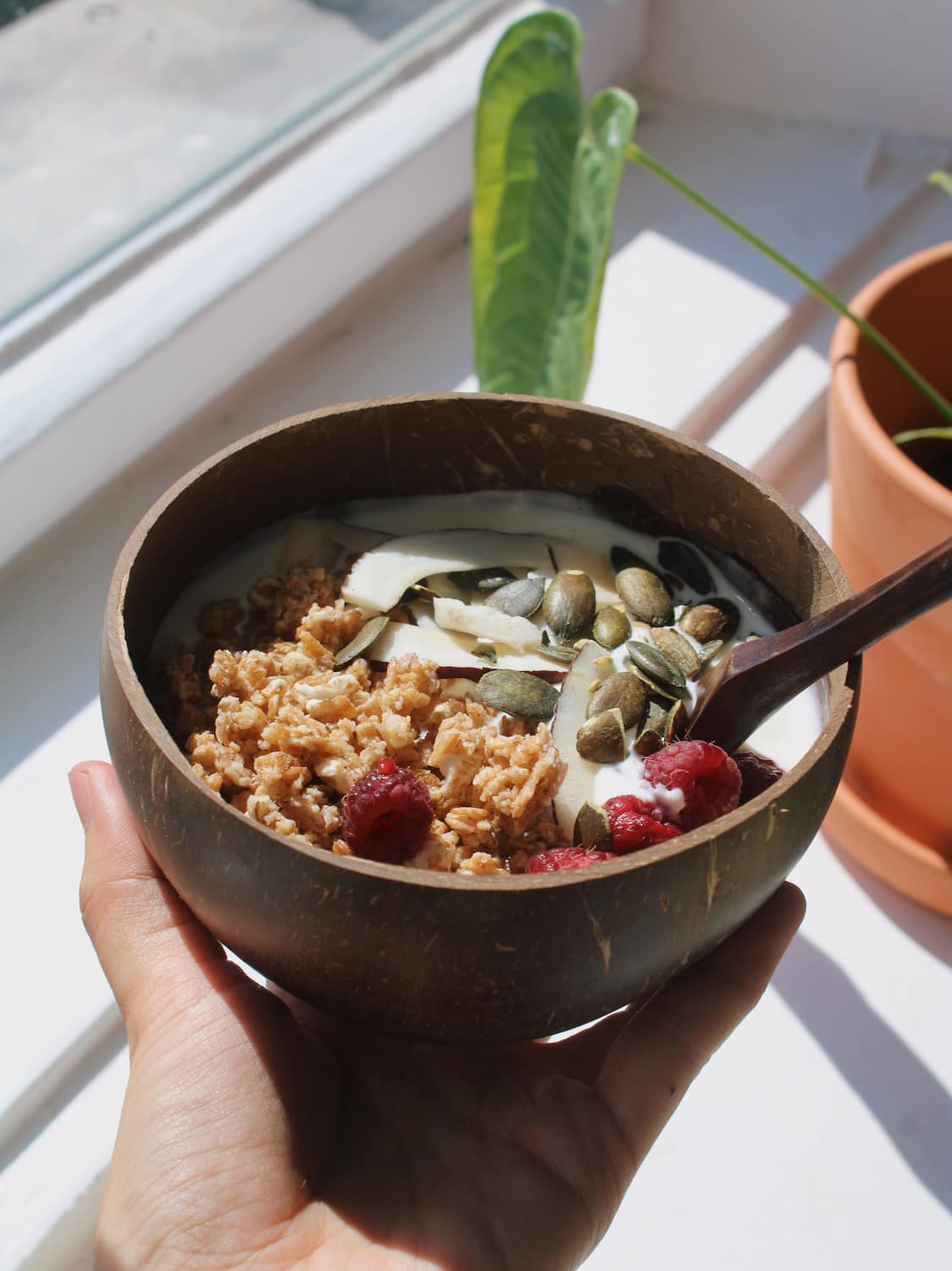 Nari coconut bowl with granola on a striped table next to a stack of books