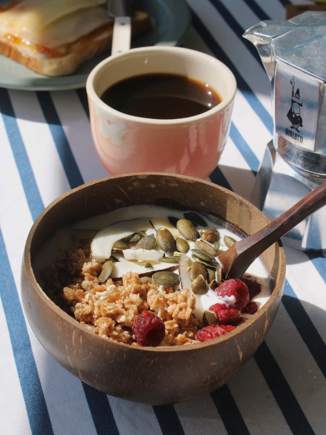 Nari coconut bowl with granola on a striped table next to a stack of books