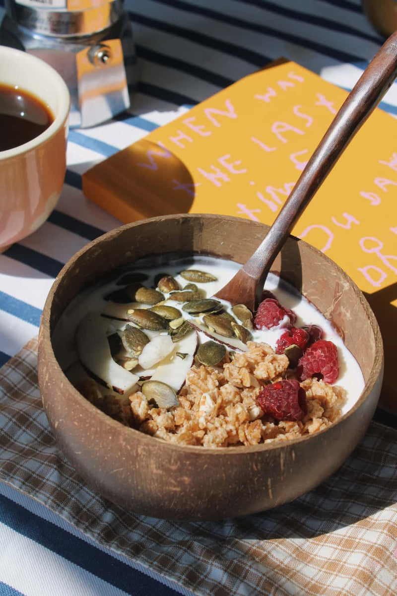 Nari coconut bowl with granola on a striped table next to a stack of books