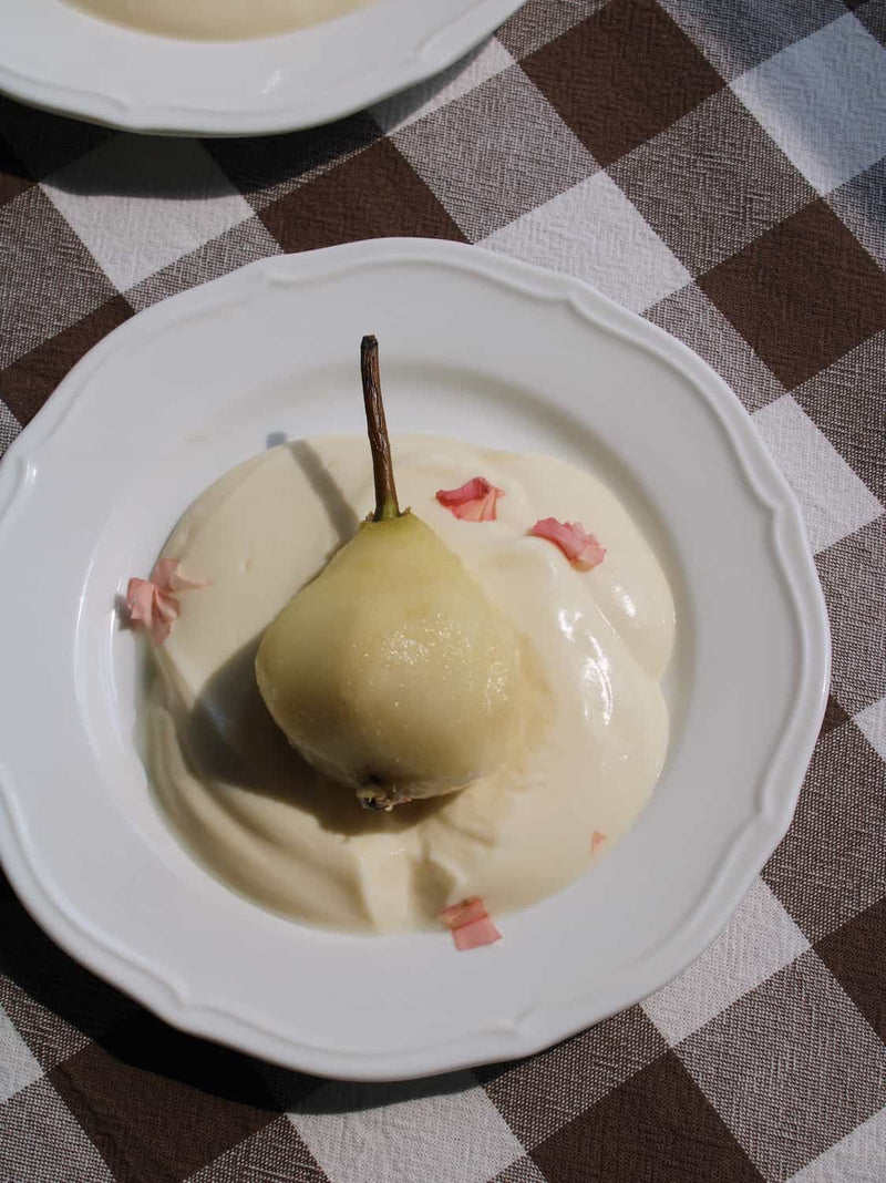 Odette white ceramic dinner plate with scalloped rim detail, styled with poached pear in cream sauce and rose petal garnish