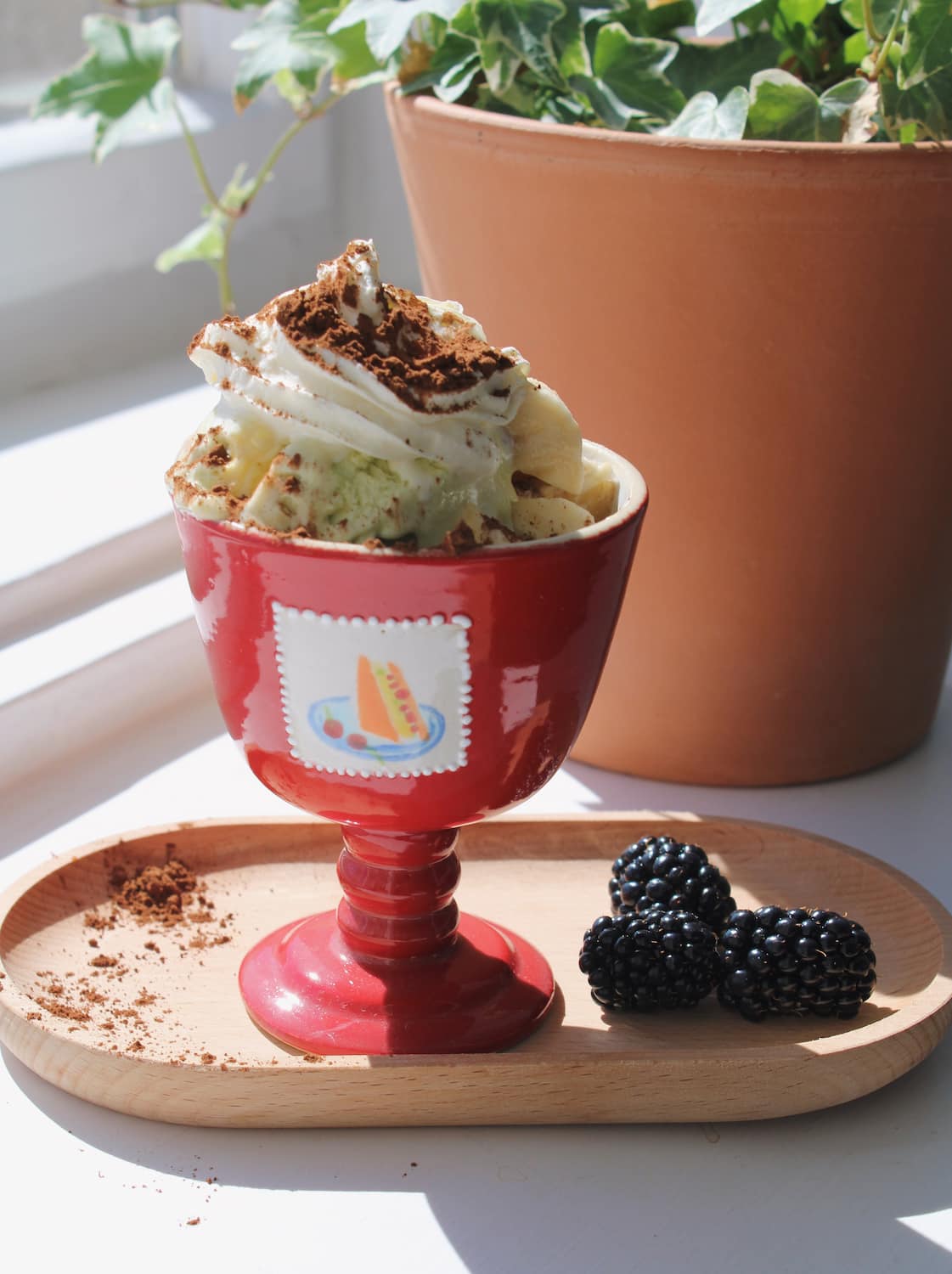 Red ceramic goblet with ice cream sundae with a cherry on top on a metal stand.