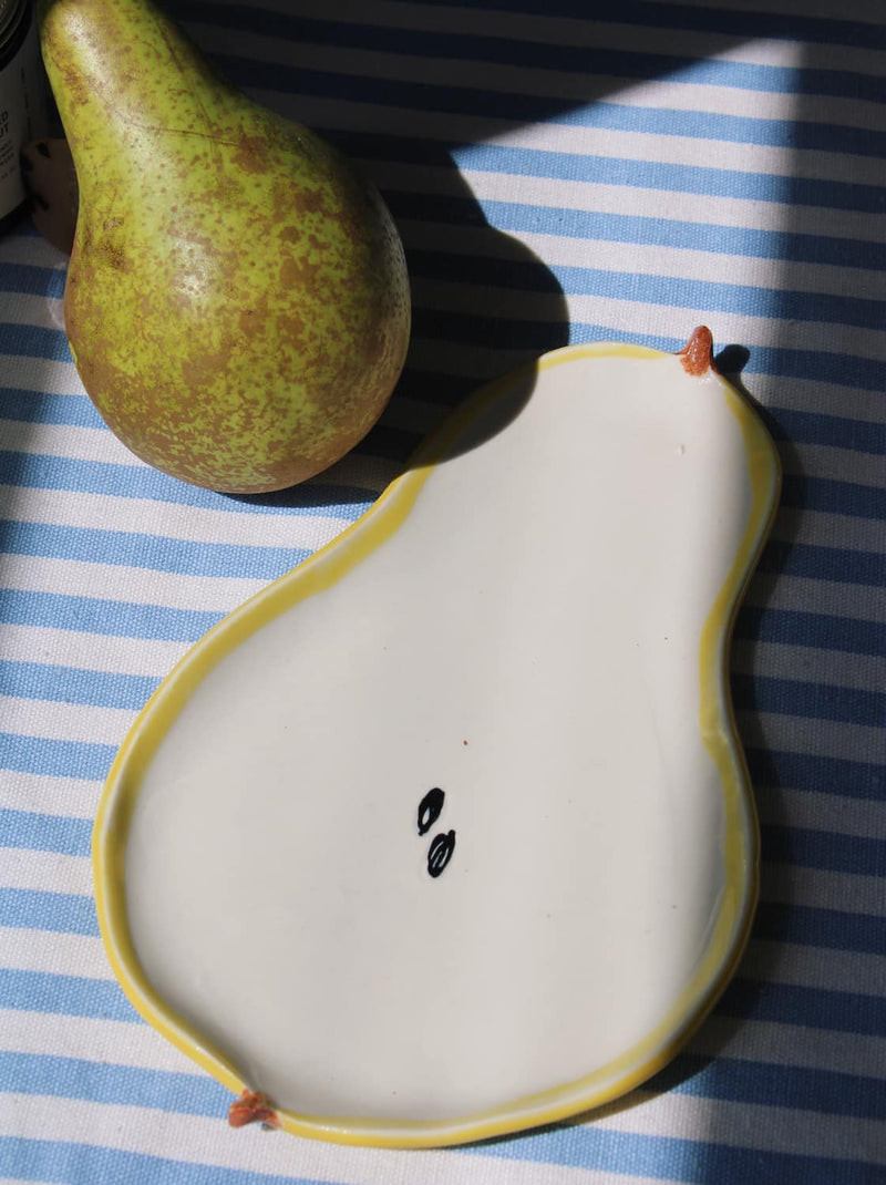 Pear-shaped ceramic spoon rest with a pear on a blue and white striped surface