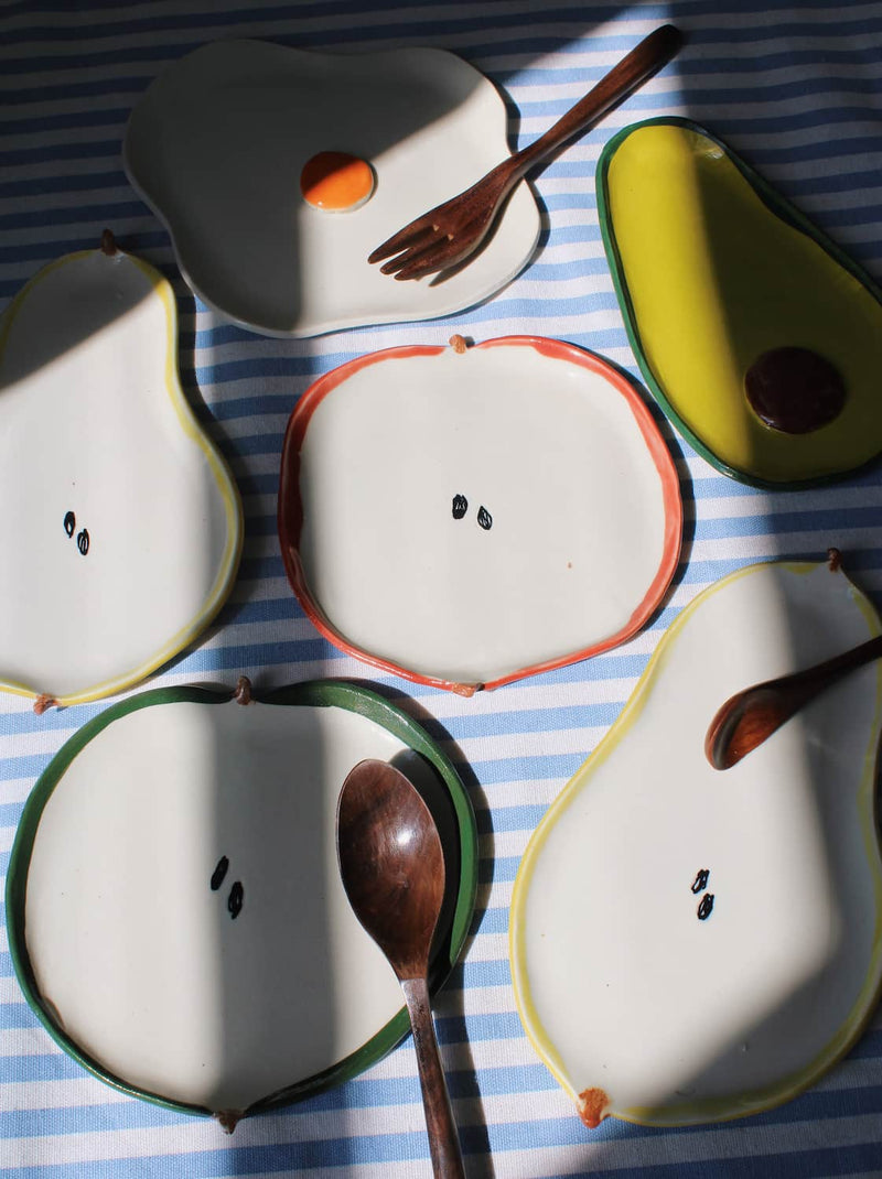 Set of ceramic fruit-shaped spoon rests with spoons on a striped tablecloth