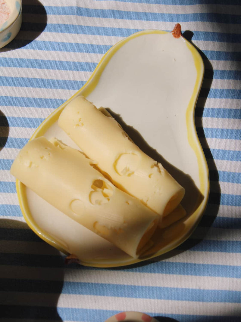 Pear ceramic spoon rest with cheese curls and tableware in warm sunlight