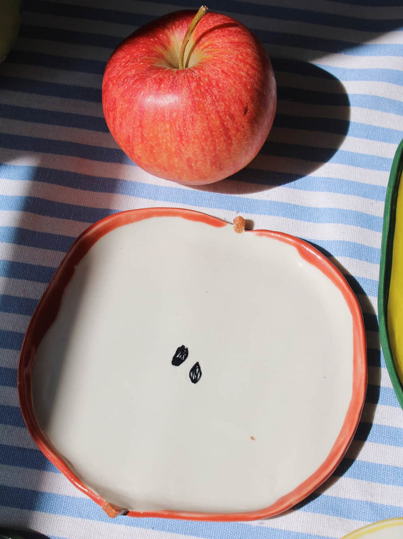 Red apple ceramic spoon rest with playful fruit shape on blue striped tablecloth