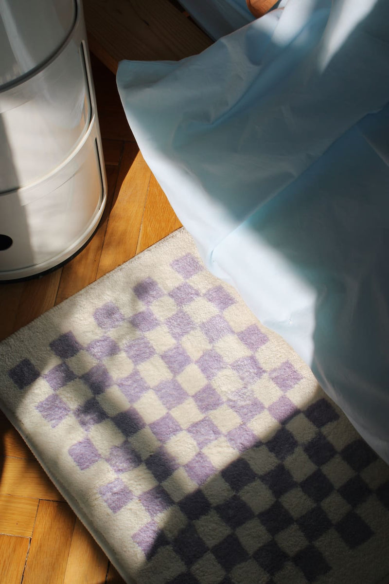 Checkered bath mat on a wooden floor with a white appliance in the background
