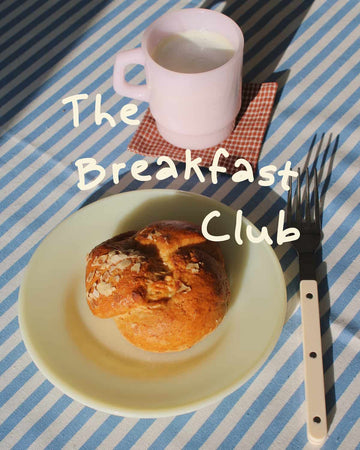 Breakfast setting with a croissant, mug, and fork on a striped tablecloth.